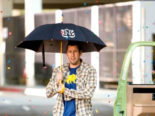 Adam Sandler holding a black umbrella while colorful confetti falls around him on the street, 2K Desktop Wallpaper