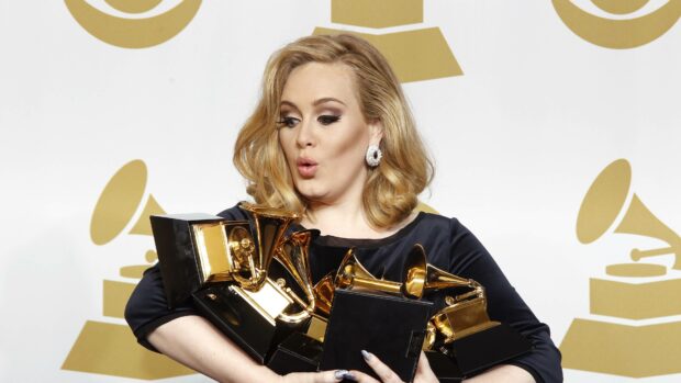 Adele holding several Grammy awards with a surprised expression on her face, 4K Desktop Wallpaper