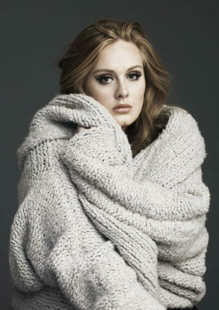 Adele Wallpapers showing a woman wrapped in a thick knitted sweater with a serious expression, 2K Mobile Wallpaper