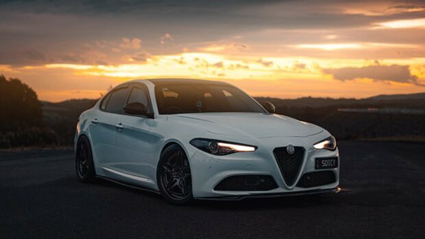 A white Alfa Romeo car is parked on a road during sunset with glowing headlights, HD Desktop Wallpaper