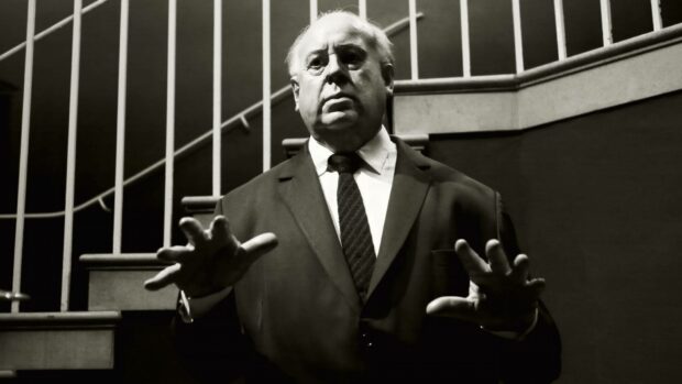 Alfred Hitchcock standing with hands raised near a staircase, HD Desktop Wallpaper