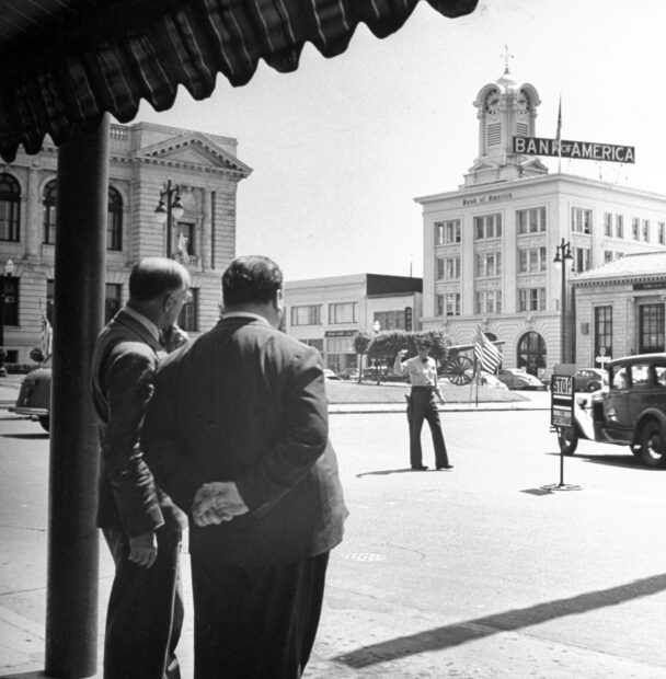 Alfred Hitchcock directs a scene on a city street with two men observing