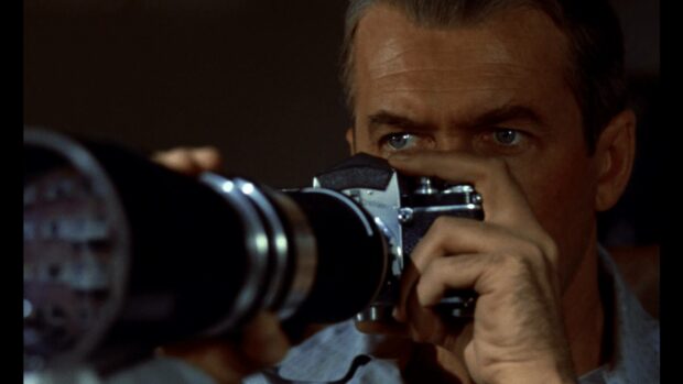 A man intensely looks through the lens of a vintage camera in a suspenseful scene, HD Desktop Wallpaper