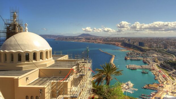 A panoramic view of a coastal city in Algeria with a domed building and harbor under a blue sky, HD Desktop Wallpaper
