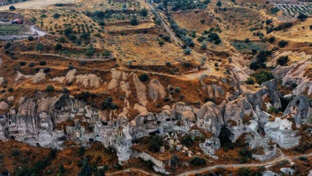 The ancient rock dwellings in Cappadocia surrounded by dry landscape and scattered trees, 4K Desktop Wallpaper