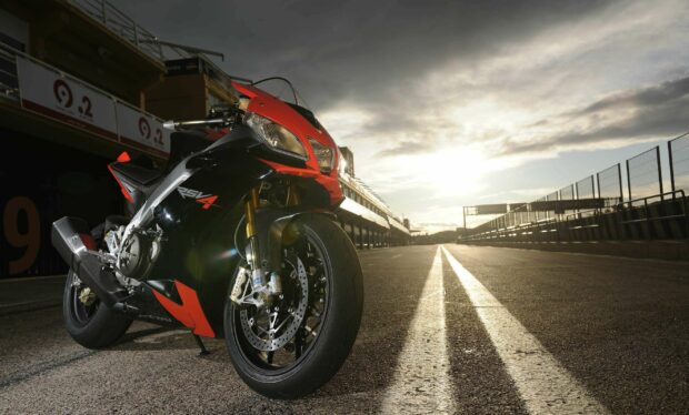 An Aprilia motorcycle is parked on a race track under a cloudy sky, 2K Desktop Wallpaper