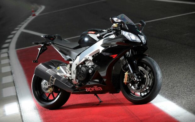 An Aprilia motorcycle is parked on a racetrack with red and black markings clearly visible, 2K Desktop Wallpaper
