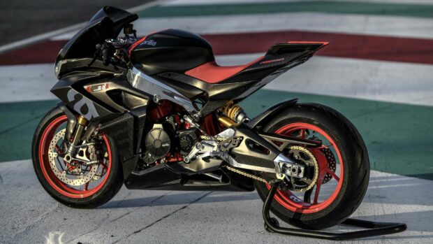 A detailed Aprilia superbike parked on a race track with red rims and carbon fiber parts, 2K Desktop Wallpaper