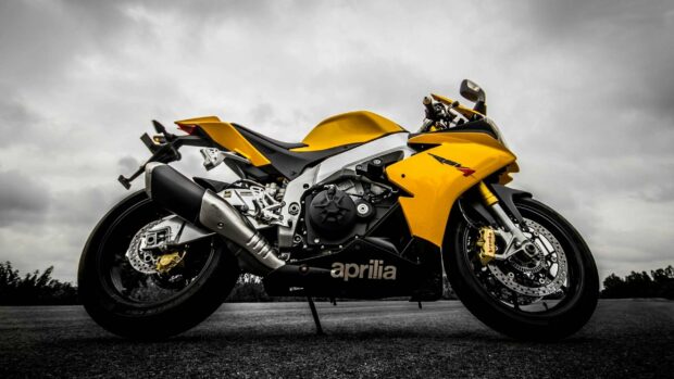 A yellow Aprilia sport bike is parked on a road under a cloudy sky, 2K Desktop Wallpaper