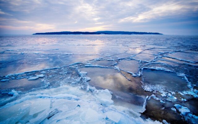 Arctic Ocean Frozen Landscape With Cracked Ice And Distant Island Under Cloudy Sky Wallpaper