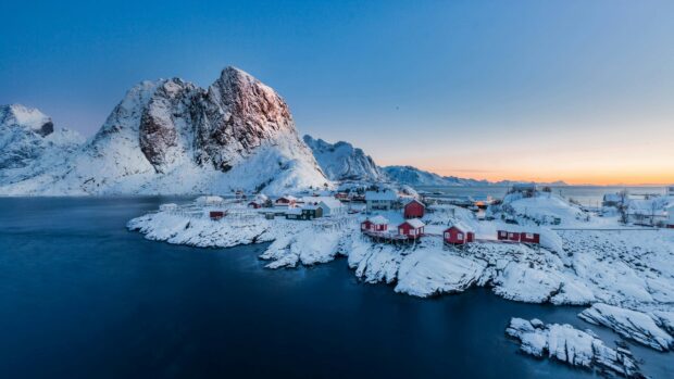 A snowy arctic village with red houses by the water and mountains under a clear sky, 4K Desktop Wallpaper