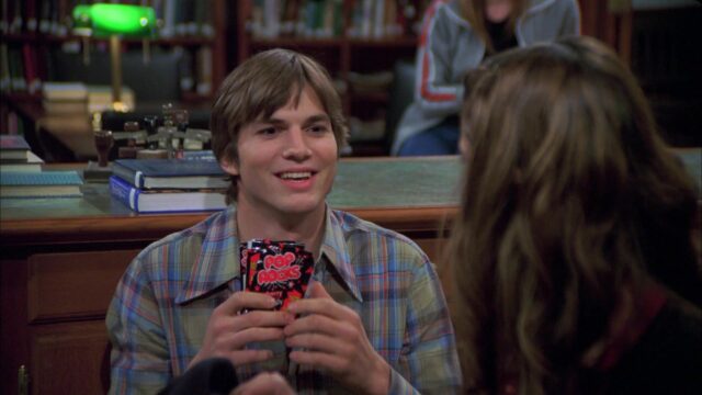 Ashton Kutcher Smiling And Holding Pop Rocks Candy In Casual Plaid Shirt Ashton Kutcher Wallpapers