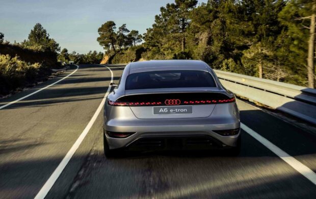 The Audi A6 e tron is shown from the rear driving on a tree lined road under clear skies, 2K Desktop Wallpaper