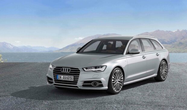 A silver Audi A6 is parked on a paved surface with mountains and a lake in the background, 2K Desktop Wallpaper