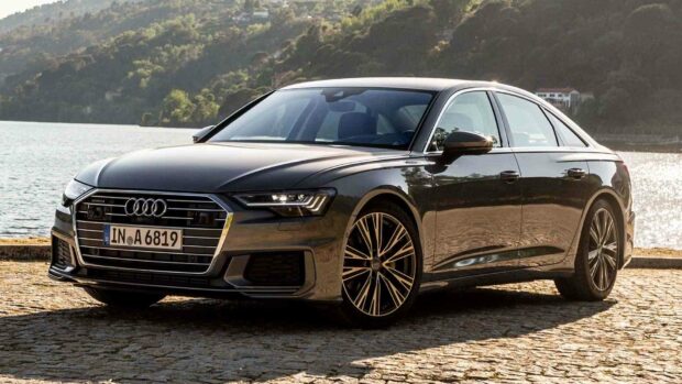 A sleek Audi A6 is parked on a cobblestone surface near a calm lake with hills in the background, HD Desktop Wallpaper