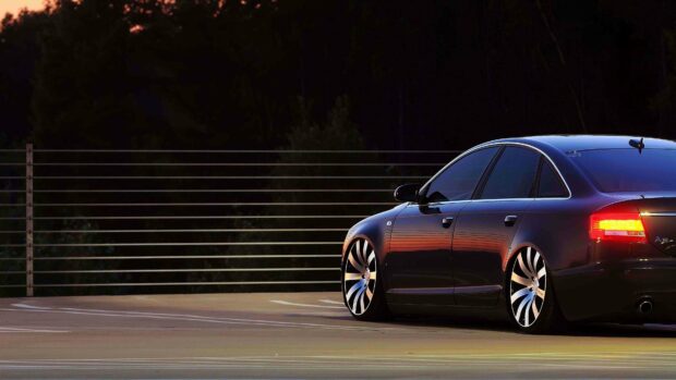 A black Audi A6 is parked near a fence with a sunset reflection on its side, 4K Desktop Wallpaper