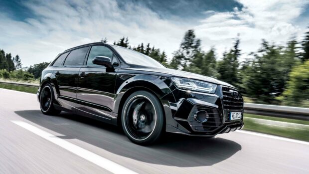 A black Audi Q7 is driving fast on a highway surrounded by trees under a cloudy sky, 4K Desktop Wallpaper