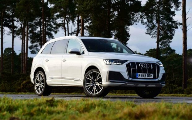 A white Audi Q7 is parked on a road surrounded by tall trees under a cloudy sky, 2K Desktop Wallpaper