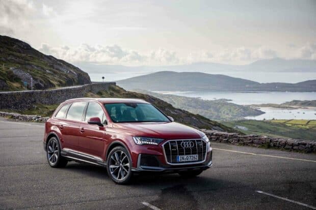 A red Audi Q7 is parked on a mountain road with hills and water in the background, 2K Desktop Wallpaper