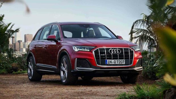 A red Audi Q7 is parked on a dirt path surrounded by greenery with a city skyline in the background, HD Desktop Wallpaper