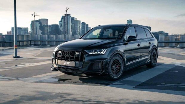 A black Audi Q7 is parked in a rooftop city parking lot with modern buildings in the background, HD Desktop Wallpaper