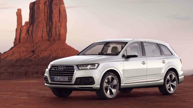 A white Audi Q7 is parked in front of a large red desert rock formation during sunset, 4K Desktop Wallpaper
