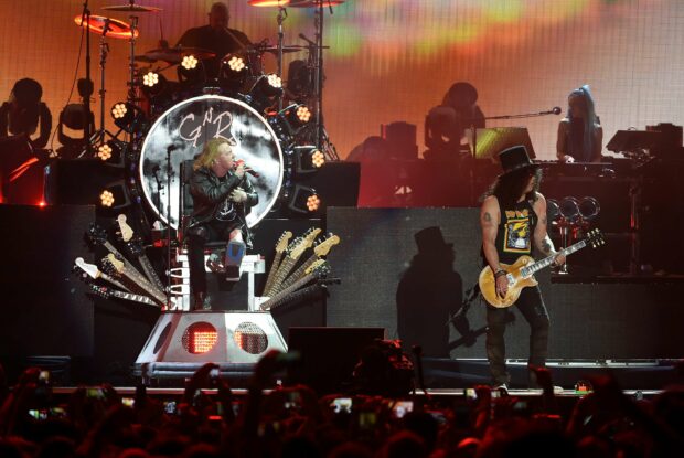 Axl Rose is singing on stage during a concert surrounded by band members and musical instruments, 2K Desktop Wallpaper