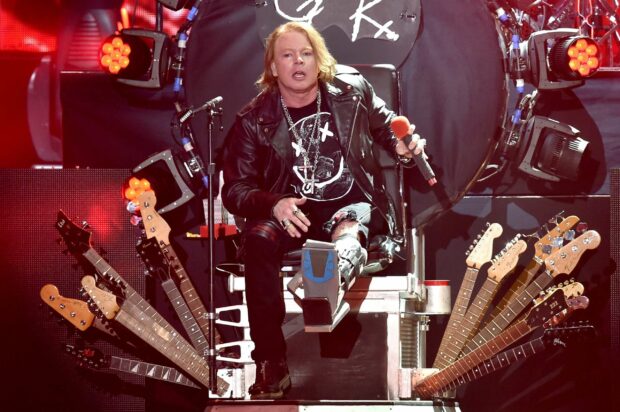 Axl Rose is singing on stage surrounded by multiple guitars and red lighting effects, 2K Desktop Wallpaper