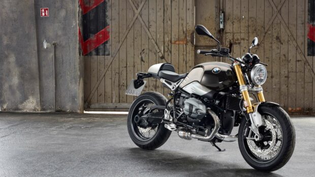 A BMW R Nine T motorcycle is parked inside an industrial garage with wooden doors in the background, 4K Desktop Wallpaper