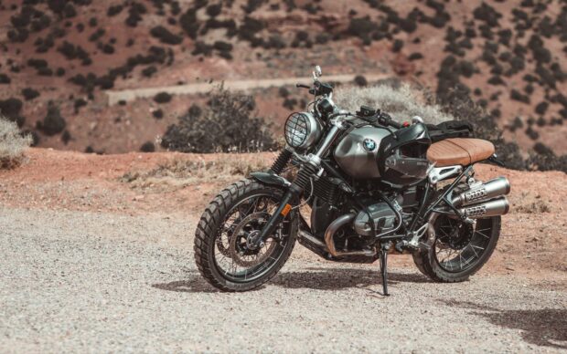 A BMW R Nine T motorcycle is parked on a gravel path in a rugged desert landscape, 2K Desktop Wallpaper