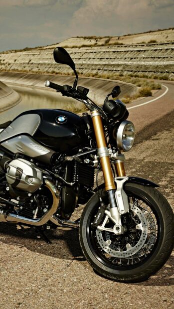 A BMW R Nine T is parked beside a curved road with a rocky embankment in the background, 2K Mobile Wallpaper