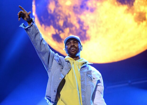 Big Sean is performing on stage wearing a yellow hoodie and denim jacket under a large illuminated moon backdrop, 2K Desktop Wallpaper