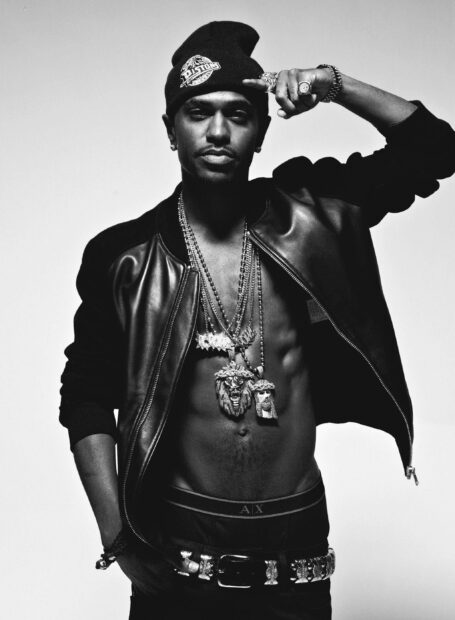 Big Sean is standing wearing a leather jacket and multiple chains while making a hand gesture on his head, 2K Mobile Wallpaper
