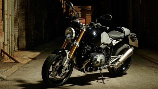 A black BMW R Nine T motorcycle is parked on a dimly lit street with brick walls in the background, 4K Desktop Wallpaper