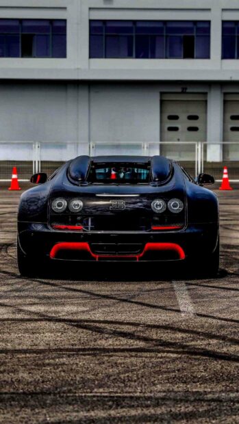 A black Bugatti Veyron with red detailing is parked on a track near a building, 2K Phone Wallpaper