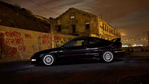 A black Honda Integra car is parked near a graffiti covered wall under a cloudy night sky, HD Desktop Wallpaper