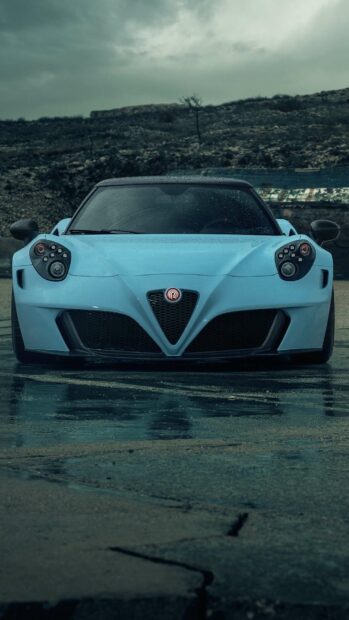 A blue Alfa Romeo car is parked on a wet pavement with hills in the background, 2K Phone Wallpaper