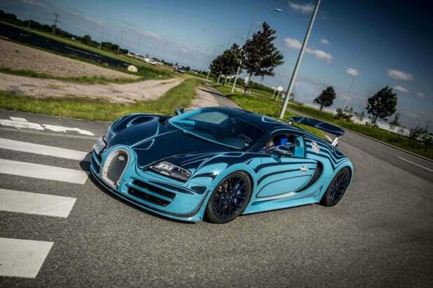 A blue Bugatti Veyron is parked on a city road with trees and streetlights in the background, HD Desktop Wallpaper