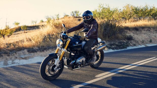 A rider is driving a BMW R Nine T motorcycle on a sunny road surrounded by dry grass and trees, 4K Desktop Wallpaper