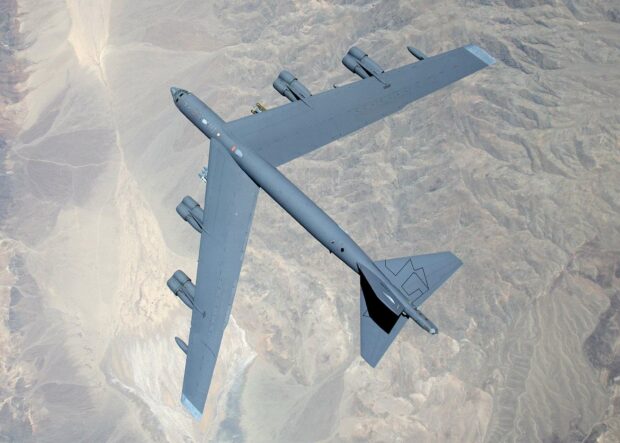 A Boeing B 52 is flying high above a vast desert landscape, showing its full wingspan and four jet engines