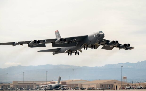 A Boeing B 52 is flying low over a military base with mountains in the background, 2K Desktop Wallpaper