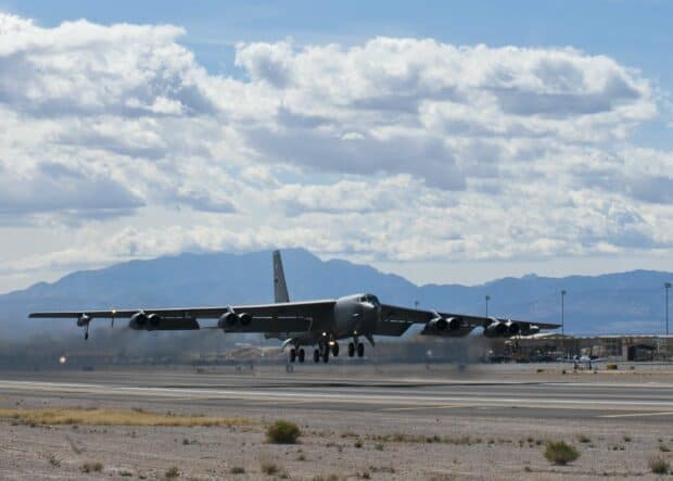 A Boeing B 52 is captured landing on a runway with mountains in the background, 2K Desktop Wallpaper