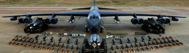 A Boeing B 52 bomber is parked on the runway with a wide array of bombs and missiles arranged in front of it