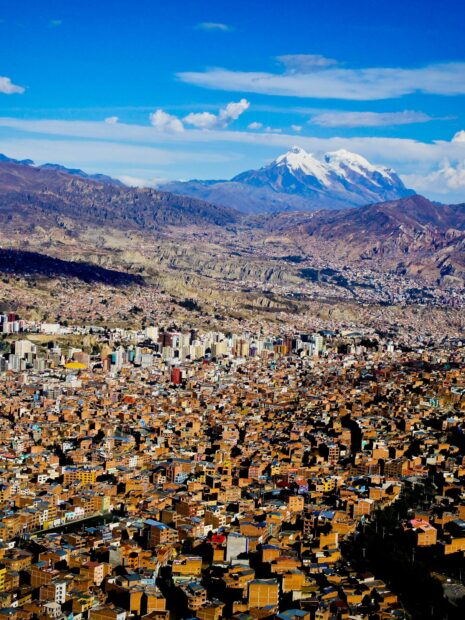 A panoramic view of Bolivia shows a dense city surrounded by mountains with snowy peaks in the background, HD Phone Wallpaper