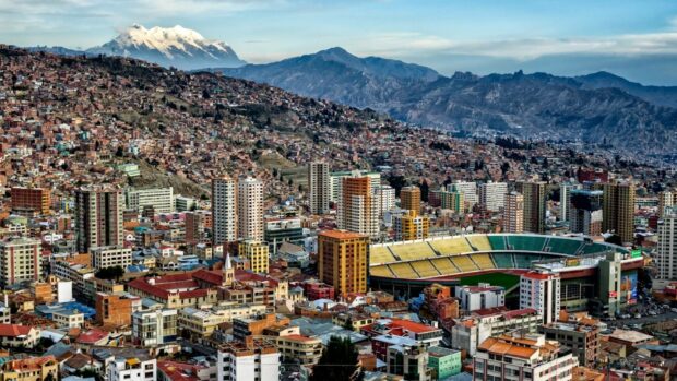 A dense cityscape in Bolivia with a stadium and snowy mountains in the background, HD Desktop Wallpaper