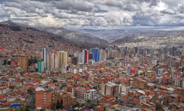 A detailed view of Bolivia cityscape shows colorful buildings and surrounding mountains under a cloudy sky, 2K Desktop Wallpaper