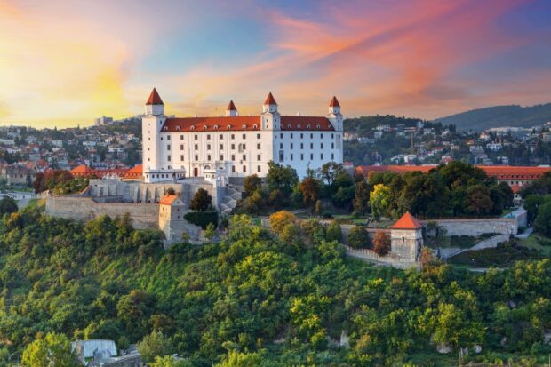 Bratislava Castle stands on a hill surrounded by lush green trees during a colorful sunset in Bratislava Wallpapers, HD Desktop Wallpaper