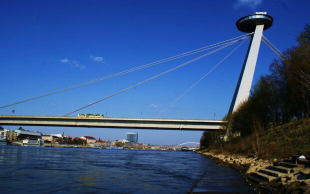 A scenic view of Bratislava with a bridge over the river and a tower under a clear blue sky, HD Desktop Wallpaper