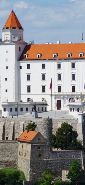 The Bratislava castle stands prominently above the city with its distinctive white walls and red roofs, showcasing Bratislava Wallpapers, 2K Phone Wallpaper