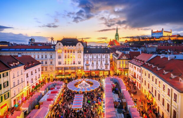 A vibrant view of Bratislava city with historic buildings and a busy market at sunset, HD Desktop Wallpaper